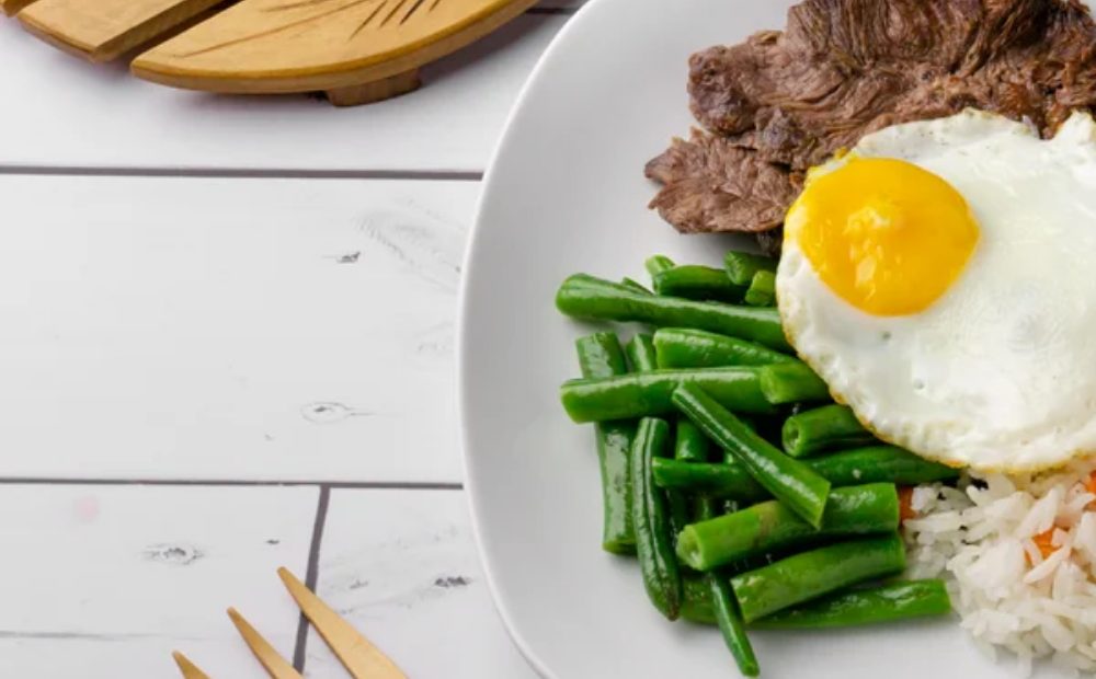 Carne asada con huevo frito, habichuelas y arroz en un plato blanco de Manzana Verde Colombia