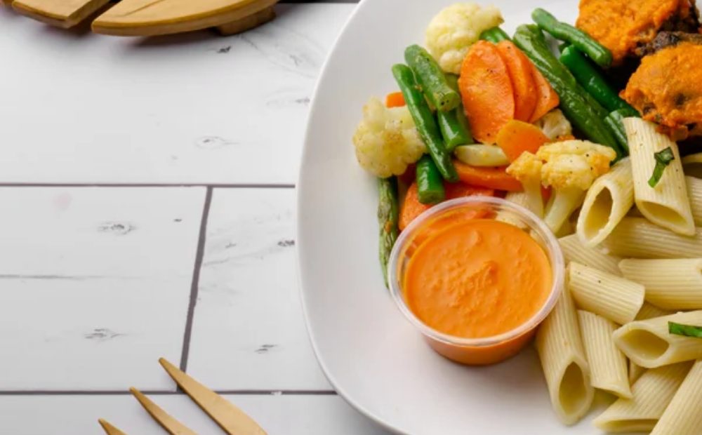 Pasta penne con verduras salteadas, croquetas y salsa en un plato blanco de Manzana Verde Colombia