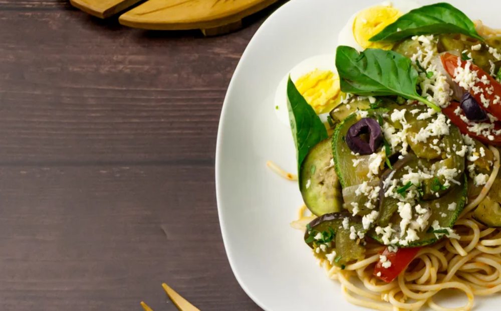 Ensalada con fideos, verduras frescas y queso servida en plato blanco