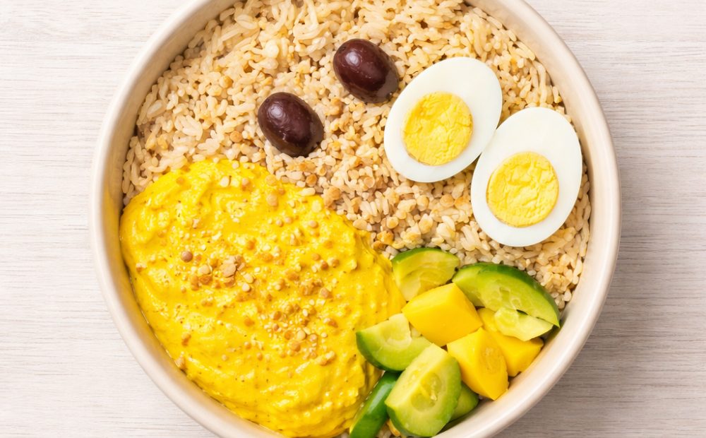 Ají de gallina con arroz integral, huevo duro, aceituna, palta y mango servido en un bowl blanco