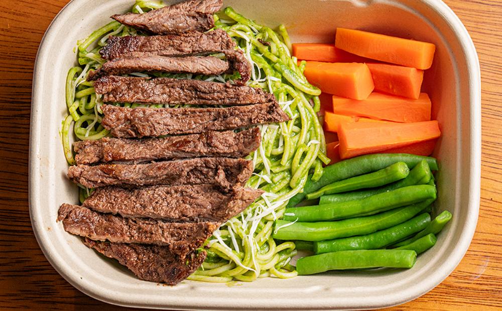 Tallarines verdes con bistec, zanahoria y vainitas servidos en el envase del menú diario de Manzana Verde